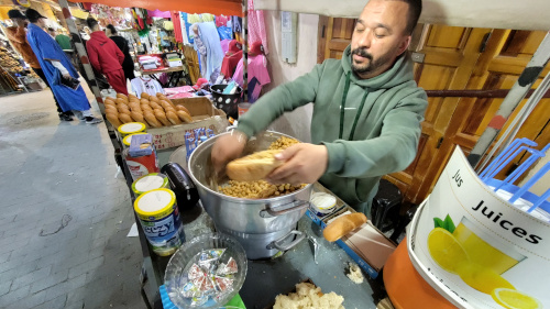 A street-food seller at his cart, scooping chickpeas into a sandwich